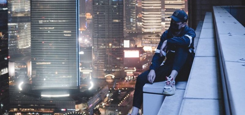 Livin' on the edge. Man sitting on building gutter at night surrounded by skyscrappers